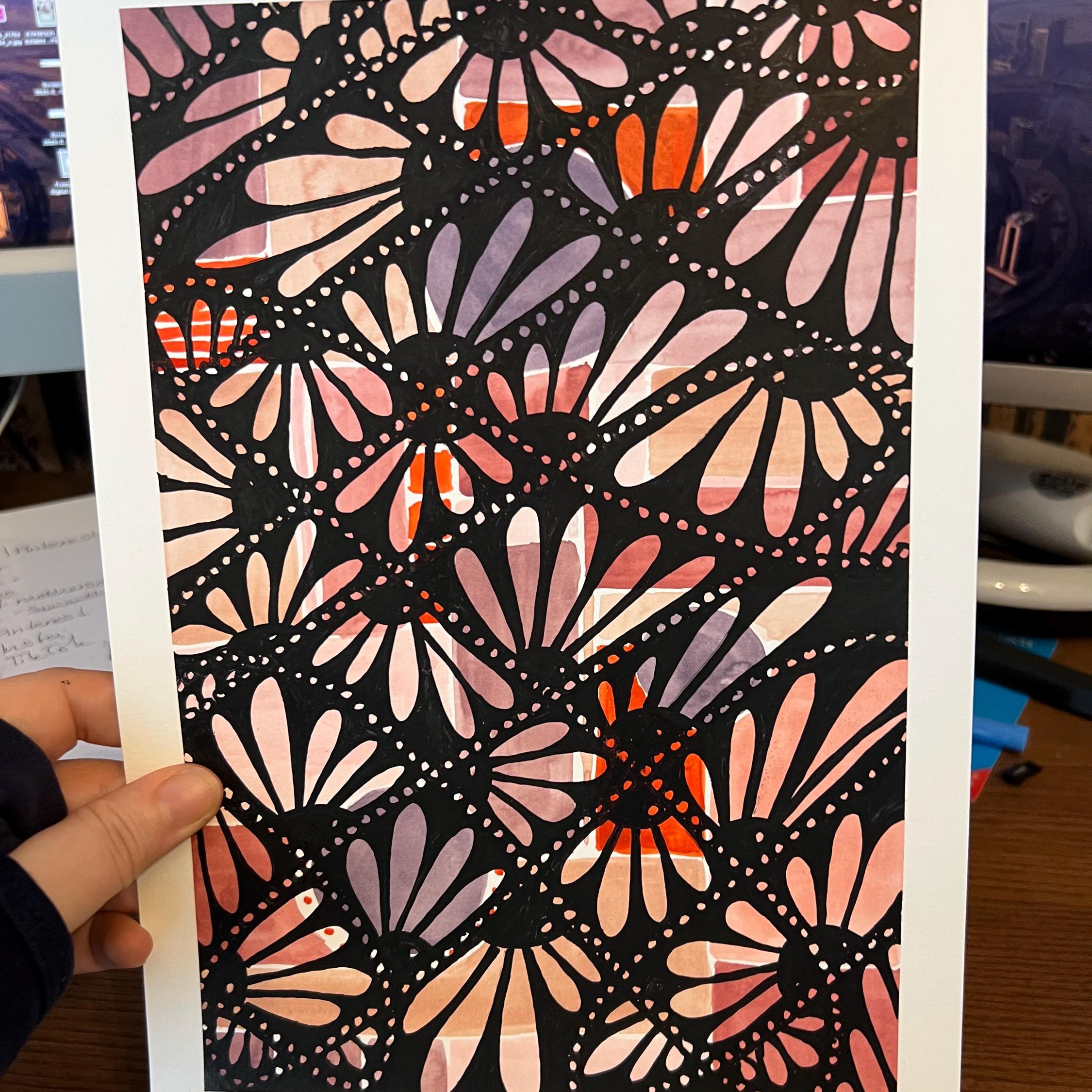 Hand holding a card with a colorful geometric pattern against a blurred indoor background