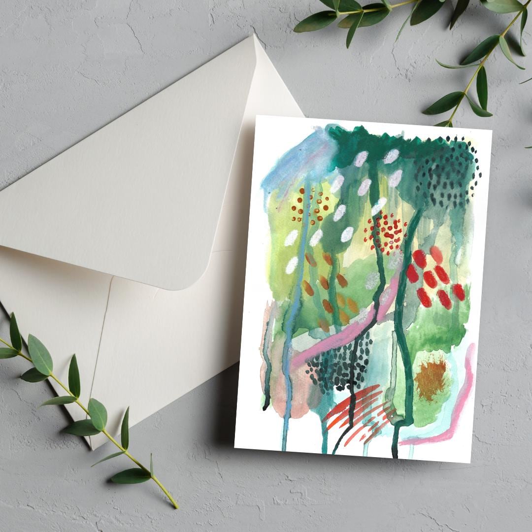 Greeting card with abstract watercolor design on a gray surface with an envelope and green leaves.